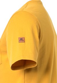 T-shirt in cotone giallo con scollo a giro, maniche corte e un'etichetta quadrata marrone con la scritta "Forsberg" sulla manica sinistra.