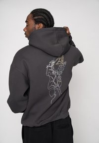 Schwarzer Hoodie mit einem großen, mehrfarbigen Schmetterlingsmotiv und Linienkunst-Design auf der Rückseite. Hergestellt aus weichem Stoff mit einer lockeren Passform.