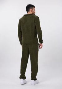 Olivegrøn, blød jogger-sæt bestående af en langærmet top og matchende bukser. Hvide sneakers fuldender looket.
