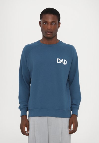 Hanorac albastru cu guler rotund ribbed, mâneci lungi și text alb "DAD" pe partea stângă a pieptului. Prezintă o textură moale și o croială lejeră.