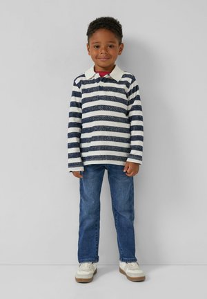 Gestreepte langemouwen shirt in marineblauw en wit met een witte kraag, gecombineerd met een blauwe jeans en witte sneakers met beige accenten.
