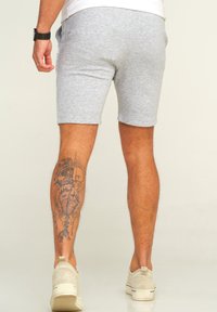 Graue Baumwoll-Mischungs-Shorts mit schmalem Schnitt, seitlichen Taschen und sichtbaren Nähten. Tanfarbenes Wildleder-Slipper vervollständigen das Outfit.