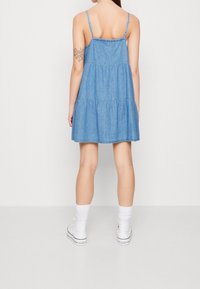 Vestido de mezclilla con un diseño de volantes, tirantes ajustables y de color azul claro. Llevado con zapatillas altas blancas y calcetines.