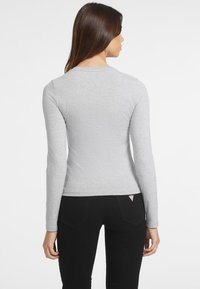 Pilkas ilgomis rankovėmis marškinys, pagamintas iš švelnios medžiagos, su apvaliu iškirpimu ir aptemptu siluetu, derinamas su juodomis kelnėmis.