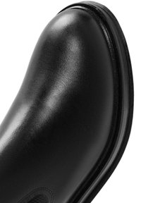 Botte en cuir noir à texture lisse, bout arrondi et surpiqûres contrastées le long de la semelle. Le design présente une finition polie.