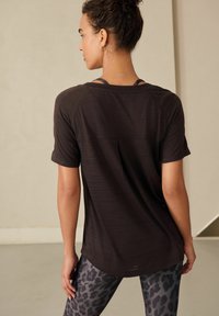 Zwarte sportT-shirt met korte mouwen, gestructureerde stof en een relaxte pasvorm, gecombineerd met grijze legging met luipaardprint.