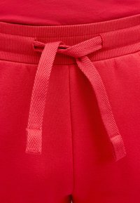 Nahaufnahme von roten Jogginghosen mit einem flachen, gewebten Kordelzug und einem gerippten elastischen Bund.