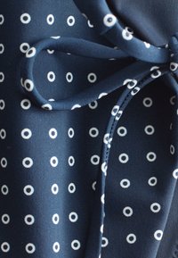 Tissu bleu marine avec motif de points blancs circulaires et nœud noué en même matière et motif.