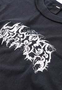 Μαύρο βαμβακερό t-shirt με μεγάλο λευκό αφηρημένο γραφικό σχέδιο με περίπλοκα μοτίβα. Κοντά μανίκια και στρογγυλή λαιμόκοψη.