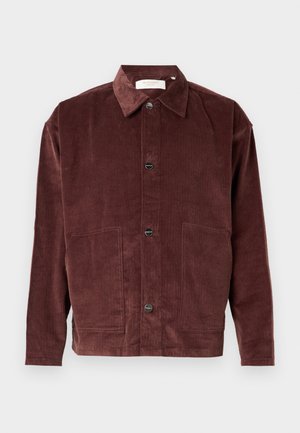 Bruine corduroy jas met een klassieke kraag, knoopsluiting aan de voorkant, twee grote zakken en geribbeld textuur.