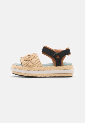 Platform sandals with woven tan upper, black adjustable strap, and braided jute sole. Features a circular accent on the strap.