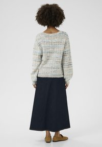 Neulepusero, jossa on pehmeä, teksturoitu kuvio pastellisävyissä ja tummansininen maksihame. Suede-lasisandaalit viimeistelevät asun.