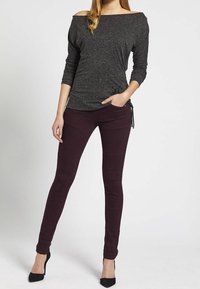 Dark gray off-shoulder top with long sleeves, paired with fitted burgundy pants featuring textured knee accents. Worn with black high heels.