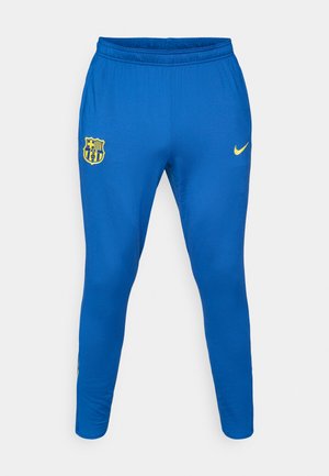 Pantalones deportivos azules hechos de tela suave, con un logo amarillo de Nike en el lado derecho y un escudo amarillo del FC Barcelona en el izquierdo.