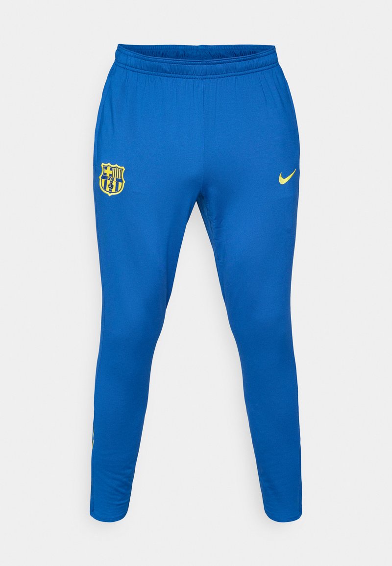 Blaue Sporthose aus glattem Stoff, mit einem gelben Nike-Logo auf der rechten Seite und einem gelben FC Barcelona-Wappen auf der linken Seite.