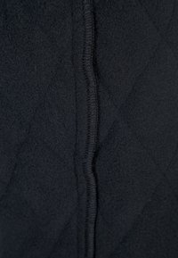 Czarna pikowana tkanina o miękkiej fakturze, z widocznym przeszyciem wzdłuż szwu. Wzór obejmuje romby rozmieszczone na całej powierzchni.