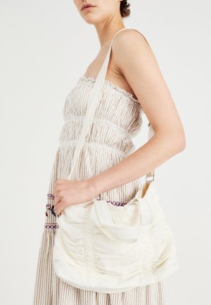Geantă de umăr din țesătură albă, cu textură gathered, curea ajustabilă și accesorii din argint. Afișată alături de o rochie de culoare crem.