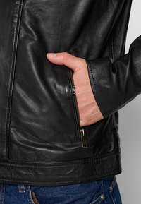 Veste en cuir noir avec une poche zippée sur le côté gauche, texture lisse, design ajusté et ourlet droit.