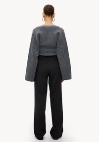 Grijze, textuur-geweven trui met wijde mouwen en een cropped ontwerp, gecombineerd met hoge zwarte broeken. Eenvoudige, strakke lijnen door het geheel.