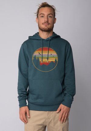 Teal hoodie met een circulaire grafiek met horizontale strepen in oranje, geel en rood, op de achtergrond van silhouetten van bomen en bergen.