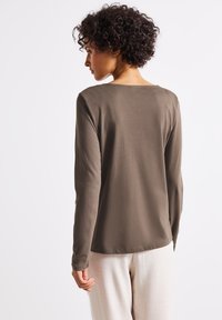Long-sleeve top in olive green jersey fabric, features a round neckline and smooth texture, paired with light-colored pants.