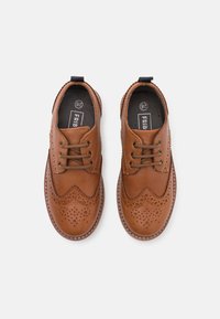 Scarpe in pelle marrone con perforazioni decorative e design a punta delle ali. Punta arrotondata, chiusura con lacci e suola a contrasto. L'interno presenta il marchio.