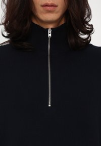 Maglione navy a costine con colletto alto e una zip argentata a metà del davanti. Il tessuto è morbido al tatto e ha una vestibilità elastica.