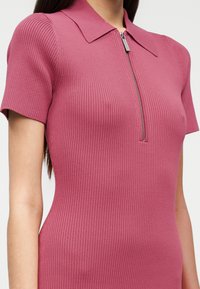 Ριμπ φόρεμα σε ροζ απόχρωση με κοντά μανίκια και γιακά, διακοσμημένο με φερμουάρ μπροστά. Το ύφασμα έχει λεία υφή και εφαρμοστή γραμμή.