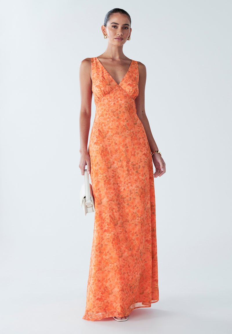 Pikk, ilma varrukateta kleit erksas oranžis, lillemustriga, V-kaelusega ning voolava kangaga. Kaunistatud väikese valge käekotiga.