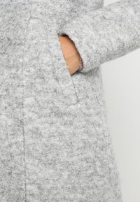 Cappotto grigio strutturato con una finitura morbida, dotato di una tasca nascosta, manicotti leggermente larghi e una vestibilità su misura.