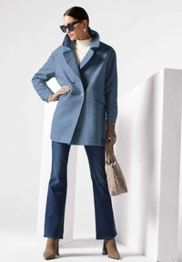 Blauwe wollen blend jas met dubbelgeknoopte knopen, grote kraag en zijzakken, gecombineerd met donkere jeans, beige handschoenen en een gewatteerde tas.