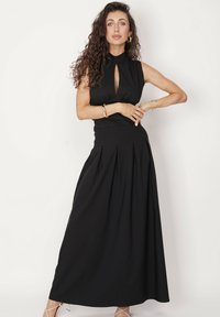 Czarna, bezrękawnikowa sukienka maxi z wysokim dekoltem i detalem w postaci otworu, z dopasowaną górą i plisowaną pełną spódnicą. Gładka faktura materiału.