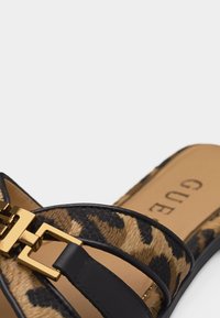 Πέδιλο με ανοιχτά δάχτυλα, λουράκι με λεοπάρ σχέδιο, μαύρη δερμάτινη λεπτομέρεια και πόρπη σε χρυσό τόνο πάνω σε ταμπά πέλμα με το όνομα της μάρκας.