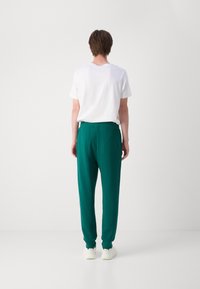 Grønne joggebukser med elastisk midje, med mansjetter ved anklene, kombinert med en enkel hvit t-skjorte, sett fra baksiden.