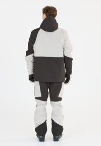 Veste et pantalon de ski imperméables en noir et gris clair. Comprend une capuche, des blocs de couleur contrastante et des genoux renforcés. Tissu texturé.