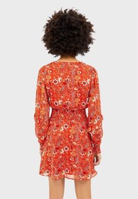 Rode jurk met lange mouwen, gerimpelde taille en bloemen-paisleypatroon. Lichtgewicht, semi-doorzichtige stof met een vloeiende silhouet.