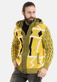 Gelbes gestricktes Kapuzenshirt mit geometrischen Schwarz-Weiß-Mustern, gerippten Kanten, einem Reißverschluss vorne und strukturierten Zopfmuster-Ärmeln.