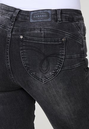 Jeans en denim noir au design ajusté, dotés d'un motif de couture en forme de papillon unique sur la poche arrière et d'une étiquette de marque au-dessus de la taille.