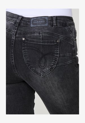 Juodi džinsai su prigludusia siluetu, turintys unikalų drugelio siuvinėjimo raštą ant užpakalinio kišenės ir prekinį ženklą virš juosmens.