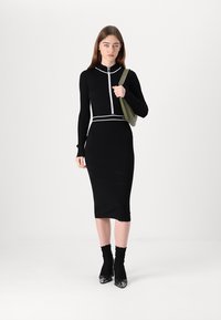 Melna ribota kleita ar pieguļošu siluetu, balta rāvējslēdzēja un akcentu kombinācija, līdz ceļiem, kopā ar melnām zeķēm un augstpapēžu kurpēm. Nenesot zaļu somu.