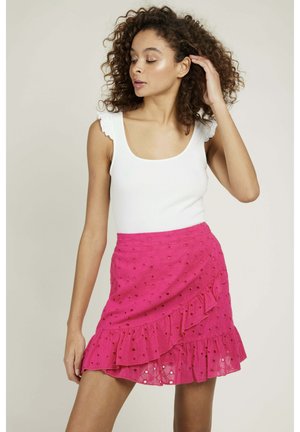 Jupe rose à volants avec découpes circulaires, fabriquée en tissu léger. Haut blanc à manches volantées porté au-dessus de la jupe. Modèle posé de profil.