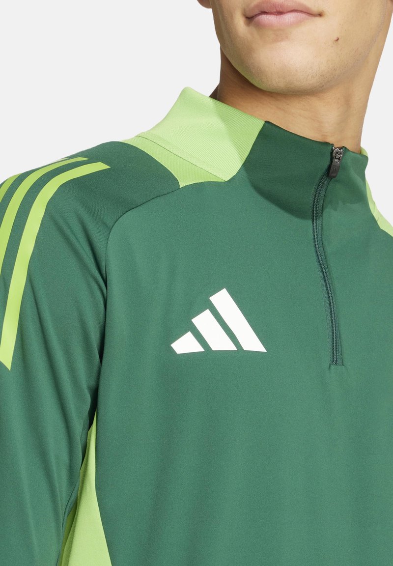 Pullover sportivo verde con mezza zip, caratteristiche accenti verde chiaro, tre strisce bianche sulla spalla e un logo Adidas sul petto.