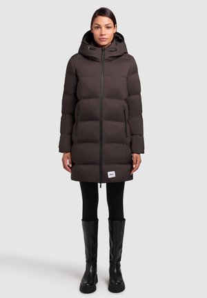 Donkerbruine gewatteerde jas met een capuchon, ritssluiting aan de voorkant, zijzakken en elastische trekkoorden, gecombineerd met zwarte legging en kniehoog laarzen.