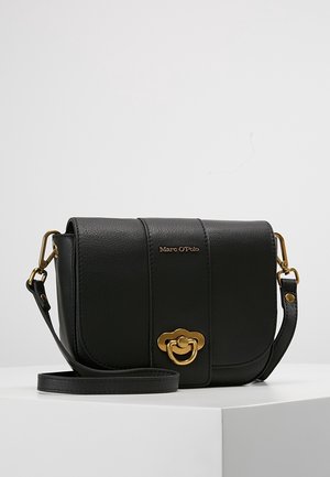 Sac bandoulière en cuir noir avec ferrures dorées, fermeture à rabat et logo "Marc O’Polo" sur le devant, posé sur une surface blanche.
