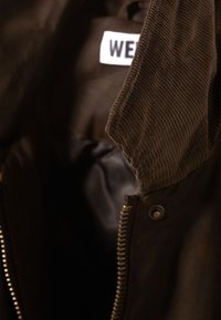 Brun kordfløjlsjakke med lynlåslukning og en glat sort inderforing. Kraven er let forhøjet og fremhæver teksturen.