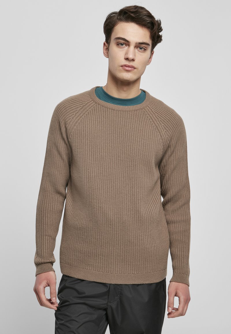 Maglione marrone a coste con scollo rotondo e maniche lunghe a raglan, abbinato a una camicia teal sotto. Il tessuto sembra testurizzato e caldo.