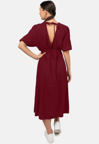 Bordeaux midi-jurk met korte puffmouwen, open rug en strikdetail. Gemaakt van gestructureerde stof, heeft een getailleerde taille en loopt vloeiend naar de zoom.