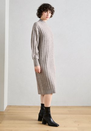 Strikket ribbet kjole i lys beige, med høy hals, lange ermer og midt på leggen lengde. Kombinert med svarte ankelstøvler.