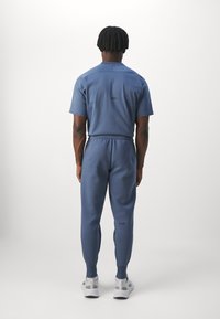 Niebieski zestaw sportowy składający się z krótkiego rękawa i zwężających się spodni, wykonany z teksturowanej tkaniny. Wyraźne logo na plecach w czarnym kolorze.