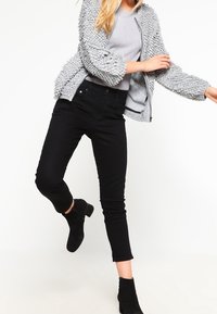 Šedý texturovaný pletený svetr se zapínáním na zip, v kombinaci s černými skinny džíny a černými kotníkovými botami. Oblečení má těsný střih a ležérní styl.